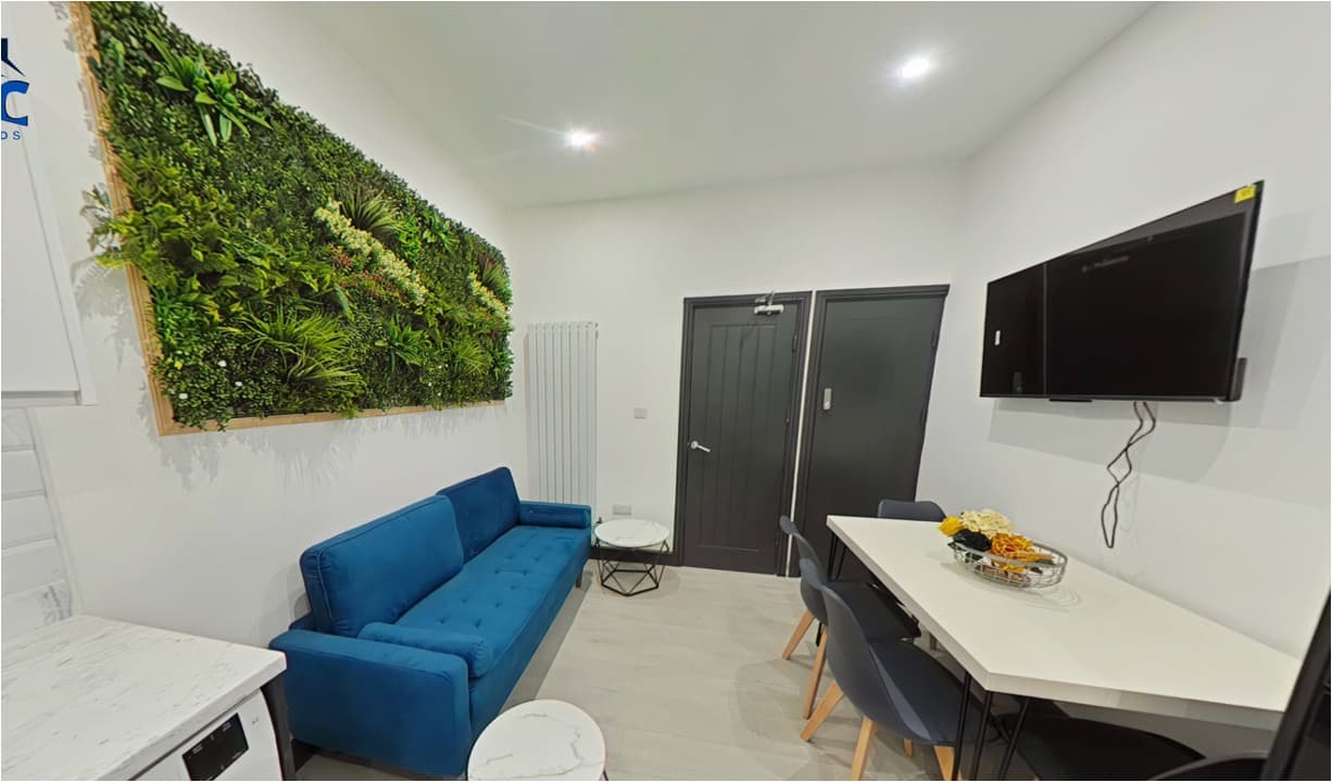 Modern living area featuring a blue sofa, lush vertical garden, and white dining table.
